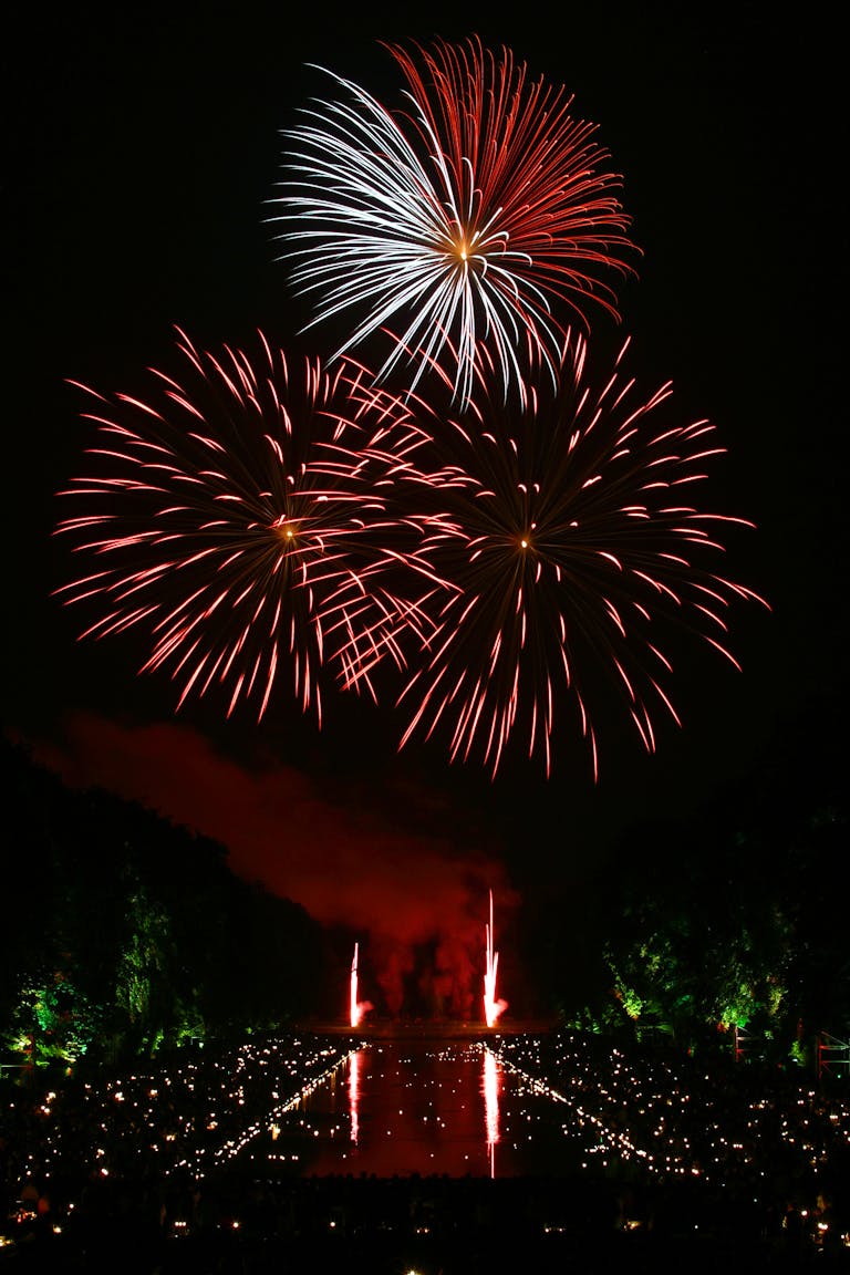 Vibrant fireworks illuminate the night sky over a reflective water surface, creating a festive atmosphere.